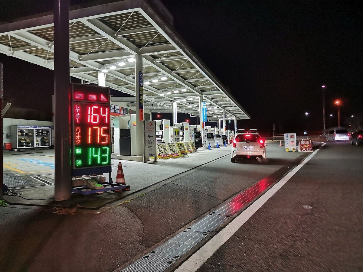 夜の給油所。電光の価格表示とセルフ式の給油機が並ぶ